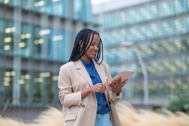 Black businesswoman smiling and working on a tablet outside a modern office building