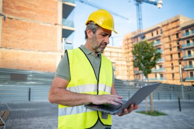 İnşaatçı inşaat alanında dizüstü bilgisayar kullanıyor