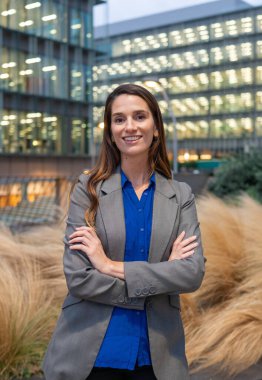 Şehirde kollarını kavuşturup gülümseyen kendine güvenen bir iş kadını.