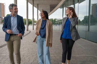 Çeşitli iş adamları yürüyor, gülümsüyor ve dışarıda konuşuyor.