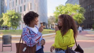 İki siyah kadın şehirde dondurma yiyip gülüyor.