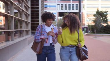 Mutlu genç bayan arkadaşlar dondurma yiyorlar. Şehirde yürüyorlar.