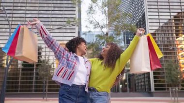 Şehirde alışveriş torbaları tutan mutlu genç bayan arkadaşlar.