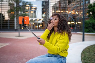 Genç bir kadın şehirde öpüşürken selfie çekiyor.