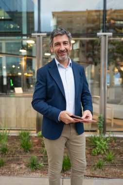 Profesyonel işadamı elinde tabletle dışarıda kameraya gülümsüyor.