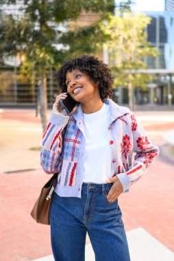 Gülümseyen siyah kadın cep telefonuyla iletişim kuruyor.