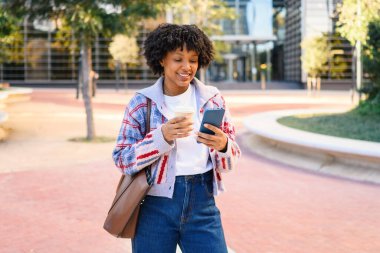 Telefonla gülümseyen, açık havada kahve içen genç bir kadın.