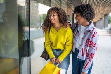 Mutlu siyah kadın arkadaşlar vitrinlere bakıyorlar.