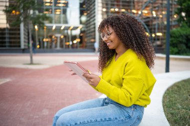 Şehirde dijital tablet kullanan gülümseyen genç bir kadın.