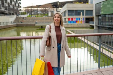 Şehirde alışveriş torbalarıyla yürüyen genç bir kadın.