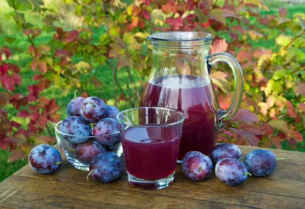 Prune juice in the carafe and glass with plums — Stock Photo, Image