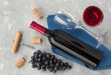 Bir şişe şarap, şarap kadehi, arka planda mavi üzüm ve tirbuşon. Üst görünüm.