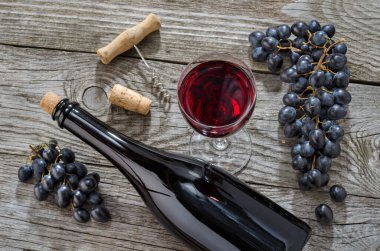 Şarap şişesi, bir bardak şarap, bir demet mavi üzüm ve gri ahşap masada tirbuşon. Üst görünüm.