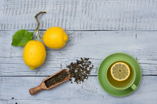 Two ripe lemons, green tea and cup of tea on blue wooden background with copy space for your text. Top view.