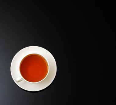 Siyah zemin üzerinde beyaz seramik çay fincanı ve metin için fotokopi alanı. Üst görünüm.