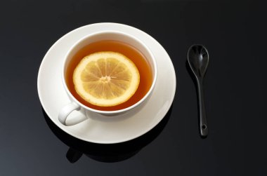 Beyaz seramik bardakta aromatik çay, koyu arka planda limonlu çay, yansımalı. Üst görünüm.