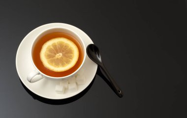 Beyaz seramik fincanın üst görüntüsü aromatik çay ile koyu arkaplanda limon ve şeker küpleri ile metin alanınız için kopya alanı.