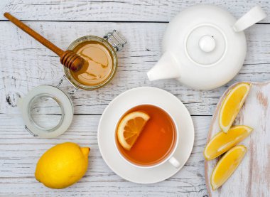 Beyaz ahşap arka planda limonlu çay, bal ve çaydanlık. Üst görünüm.