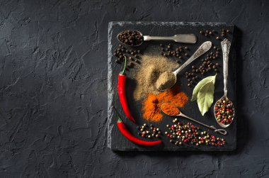 Siyah desenli arka planda klasik metal kaşıklarda çeşitli baharatlar. Metnin için en üstte boşluk var. Yemek sanatı.