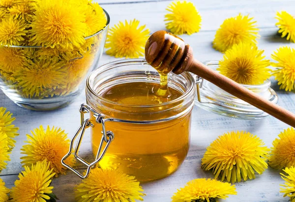 Jam of dandelions in the jar with fresh flowers on light blue wooden table. Close-up.