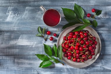 Olgun kirazlı metal tabağın üst görüntüsü ve ahşap zemin üzerinde vişneli içecek ile metin için fotokopi alanı. Düz yatıyordu.