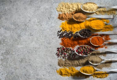 Siyah kesme tahtasındaki çeşitli baharatlar eski metal kaşıklar ve gri desenli arka plan. Metnin için alanı olan en üstteki görünüm.