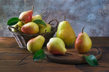 Olgun armutlar sepetin içinde ve mutfak tahtasının üzerinde tahta masanın üzerinde..