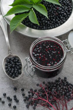 Ev yapımı reçel kavanozu ve gri taştan arka planda olgun siyah mürver. Yakın plan..