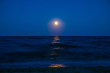 Ufukta deniz ve ay ışığı görünen manzara. Gecenin ay ışığıyla panorama. Suyun üzerindeki ay yolu. Uzun pozlama