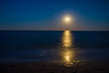 Ufukta deniz ve ay ışığı görünen manzara. Gecenin ay ışığıyla panorama. Suyun üzerindeki ay yolu. Uzun pozlama