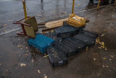Yağmurda asfaltta sebzeler ve meyveler için plastik kap yığını. Bir sürü boş plastik sandık. Asfaltta eski bir tabure var.