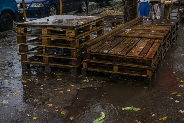 在集市附近的雨中 在沥青路面上堆满了装集装箱的木制货盘 许多空木桶 — 图库照片