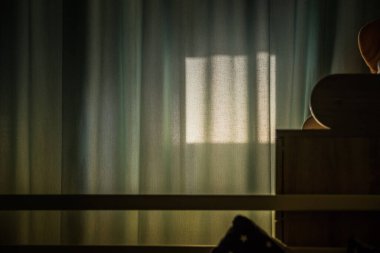 Karanlık bir odadaki perdelerin üzerindeki pencere silueti. Beyaz bir perdenin ardında güneş ışınları.