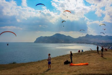 Denizin üzerinde gökyüzünde paraşütle atlıyor. Paragliderler deniz kıyısında uçar.