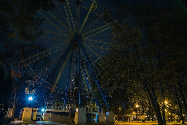 Ferris wheel in the park at night. Benches in the park during the autumn season at night. Illumination of a park road with lanterns at night.