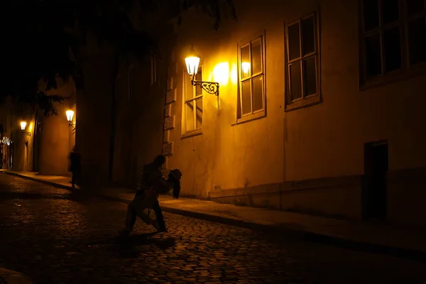 プラハの夜 街の道路の真ん中で男と女が踊っています 舗装道路で夜の光の中で踊る若いカップル — ストック写真