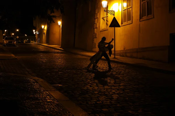 プラハの夜 街の道路の真ん中で男と女が踊っています 舗装道路で夜の光の中で踊る若いカップル — ストック写真