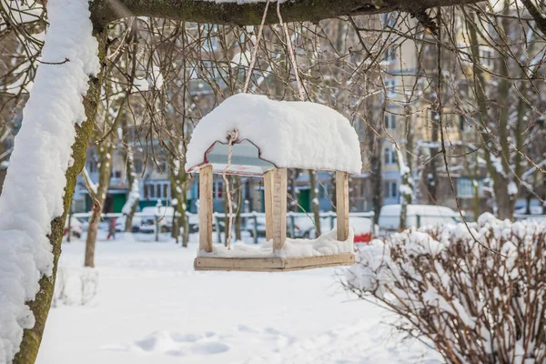 The bird feeder is covered with snow near the school. Wooden bird table topped with fresh snow