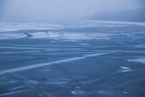 People in the middle of a frozen river. Frozen river in fog on a cloudy day. Human footprints on ice in the middle of the river. now stripes. Trees in the fog. Dnipro. Kyiv, Ukraine