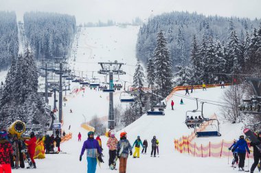 Ukrayna. Bukovel - 02 Şubat 2021. Kayakçılarla ve noel ağaçlarıyla kayak kaldırma. Asansörün bir kısmı dumanlı, kış bulutlu bir gün..