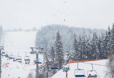 Ukrayna. Bukovel - 02 Şubat 2021. Kayakçılarla ve noel ağaçlarıyla kayak kaldırma. Asansörün bir kısmı dumanlı, kış bulutlu bir gün..
