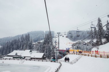 Ukrayna. Bukovel - 02 Şubat 2021. Kayakçılarla ve noel ağaçlarıyla kayak kaldırma. Asansörün bir kısmı dumanlı, kış bulutlu bir gün..