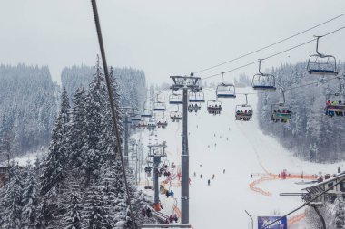 Ukrayna. Bukovel - 02 Şubat 2021. Kayakçılarla ve noel ağaçlarıyla kayak kaldırma. Asansörün bir kısmı dumanlı, kış bulutlu bir gün..