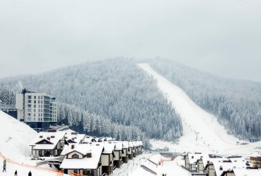 Dağlarda, kayak pistinde, teleferik ve ahşap evlerle bulutlu bir gün. Tahta evler ve karda Noel ağaçları. Karpatlar. Ukrayna