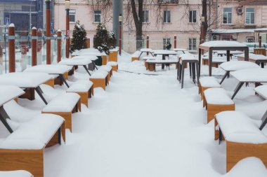 Şehir caddesinde kışın restoranın yanındaki kaldırımda karlarla kaplı masa ve banklar..