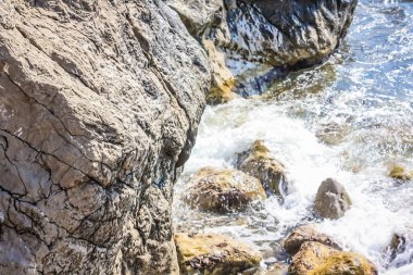 Turkuaz deniz taşı plajı, parlak güneş ışığında dalgalar kırılıyor. Renkli parlak deniz arka planı. Yaz konsepti, tatil, seyahat. Saf deniz suyu, sahilde büyük taşlar.