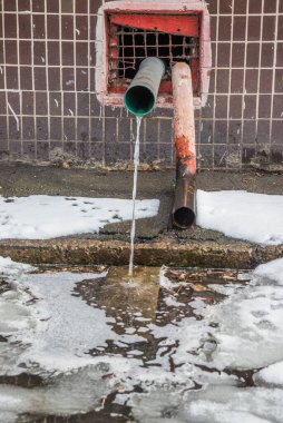 Su binanın çatısından bir drenaj borusundan akıyor. İlkbahar ve eriyen kar.