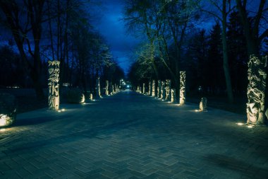 Gece parkındaki fayanslı yol lambalarla aydınlatılmış taş heykellerle dolu. Geceleri parktaki taş heykeller. Geceleri fenerlerle dolu bir parkın aydınlanması. Lutsk