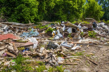 Binanın arka bahçesine inşaat enkazı saçılmış. Büyük bir şehirdeki çimlerin üzerinde çeşitli çöpler var. Yeşil ağaçların arka planında eski kutular, kontrplak ve plastik torbalar