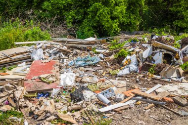Binanın arka bahçesine inşaat enkazı saçılmış. Büyük bir şehirdeki çimlerin üzerinde çeşitli çöpler var. Yeşil ağaçların arka planında eski kutular, kontrplak ve plastik torbalar